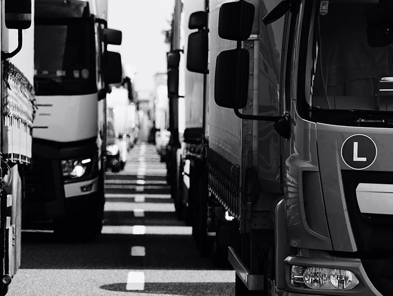 Columns of trucks on motorway in grayscale.